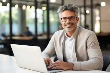 Portrait of middle-age smiling handsome business man using laptop computer, typing, working in modern office looking at camera