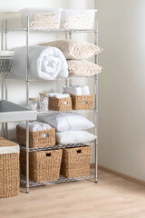 Fototapeta na wymiar Interior of Bright Modern Laundry Room with White Duvet, Towels, Cozy Pillows, and Wicker Baskets on Adjustable Metal Storage Rack with Shelves, Chrome Wire Shelving Unit, Over Wooden Flooring.