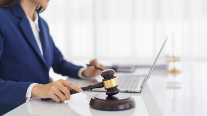 Fototapeta na wymiar Lawyer woman holding wooden judge gavel and reading business contract with law agreement on laptop