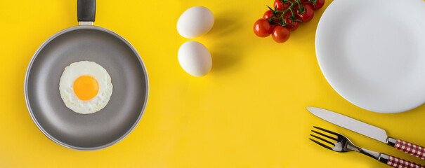 Frying pan with fried egg and  ingredients for breakfast on the yellow  background.Copy space. Top view.