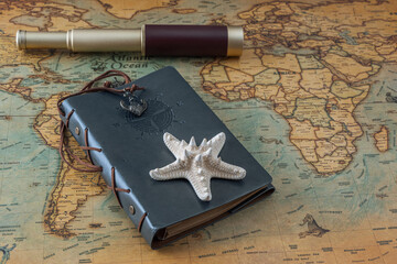 Starfish, a leather-bound book and a spyglass lie on an old map. Close-up