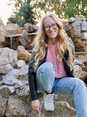 Obraz premium Natural Curly Blonde Woman, Albino Sitting Outdoors and Smiling. Lack of melanin pigment in hair and skin. A person with poor eyesight wearing glasses. Vertical