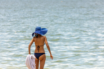 The woman wearing bikini and blue hat standing on the beach of sea to start swimming in Pattaya city in Thailand. 