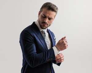 side view of sexy fashion man in suit looking down while fixing sleeves
