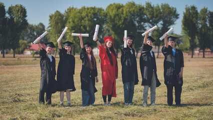 Young graduates pose and wave diplomas in their hands in the street.