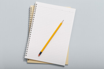 Top down view of empty light colored notebooks with pencil on colored backgrounds