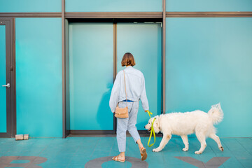 Woman with white dog entering supermarket with beautiful turquoise sliding doors. Concept of pet...