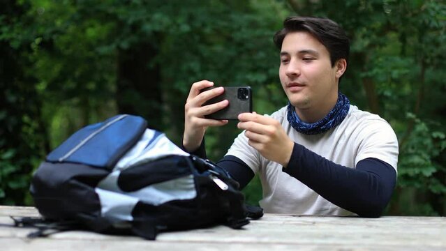 Male tourist with backpack takes pictures with smartphone landscape in forest