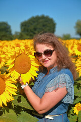 Portrait of a young woman in sunglasses on a field with sunflowers.