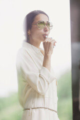 Portrait of attractive brunette holding whistle in her hand. Fashionable young woman with long hair in white costume standing in interior. Fan, coach, counselor.