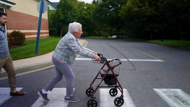 Elderly senior old woman at pedestrian crossing using walker with grandson family member outside.