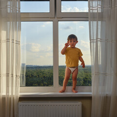 Baby is standing on the window sill, gazing out at the sky and risking a life-changing accident. ...
