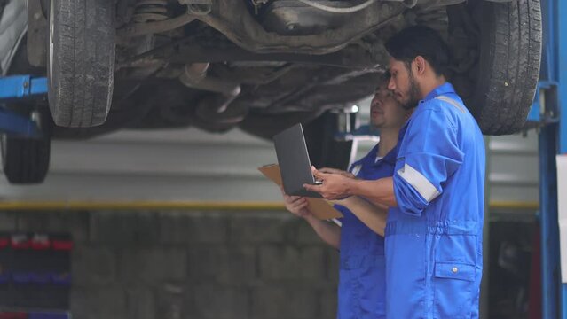 Two mechanics in a car repair shop are discussing repairs to the underbody and suspension of an old car. Auto mechanic is checking the engine's operating system.