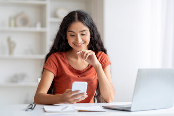 Focused young indian woman gracefully maneuvers between laptop and phone,