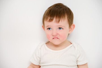 Fototapeta premium Offended baby looks pursed lips, studio white background. Sad child with the emotion of resentment on his face. Kid about two years old (one year nine months)
