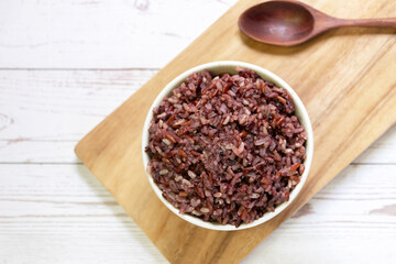 Cooked rice berry rice in a bowl with wooden spoon on wooden tray background; top view.