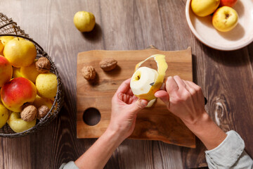 Human hands peeling an apple on a kitchen with a knife over a wooden backround