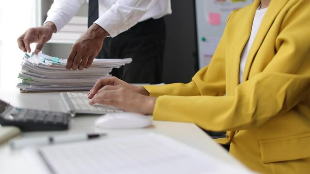 Businessman working on documents on the desk and a businesswoman working on accounting documents are typing on the computer in the office.