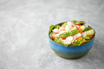 Salad with mozzarella and vegetables in homemade bowl on the table. Copy space