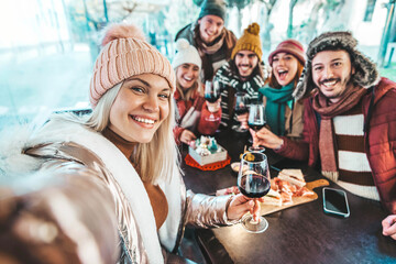 Best friends taking selfie sitting in dining restaurant table  - Group of young people at terrace party drinking red wine together - Winter season - Beverage life style concept