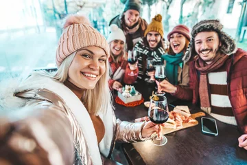 Fotobehang Best friends taking selfie sitting in dining restaurant table  - Group of young people at terrace party drinking red wine together - Winter season - Beverage life style concept © Davide Angelini