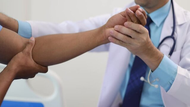 Doctor is diagnosing a male patient's arm and shoulder pain in a hospital examination room. Physical therapist testing patient's arm.