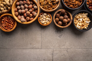 Assortment of nuts in bowls on stone background top view with copy space. Healthy snack food.