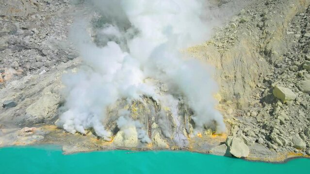 Toxic volcanic gas at the sulphur mines in the crater of the active volcano of Kawah Ijen with turquoise lake inside, East Java, Indonesia. Aerial Drone view 4K.