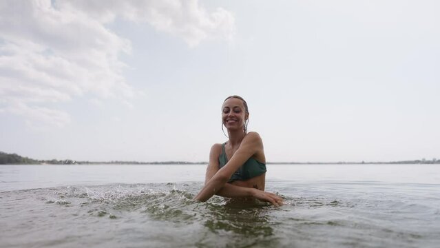beautiful joyful young sexy girl in green swimsuit having fun in lake water and splashing water by hands. Sporty body of beautiful woman in bikini on beach tropical background