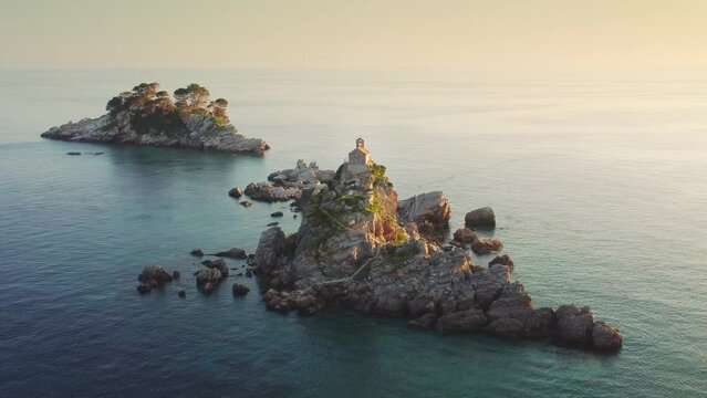 Amazing sunset aerial view from a drone of the tiny Church Sveta Nedjelja Island near Petrovac in Montenegro. Picturesque stone island and a small church on a cliff surrounded by Adriatic sea waves