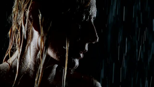 inspired pensive woman in rain or in shower in night, closeup view of face, drops falling on skin
