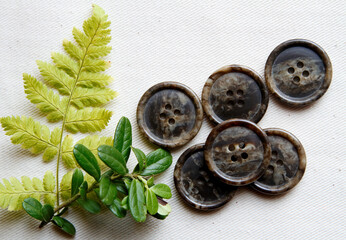 Gray and brown buttons on white textile with green leaves