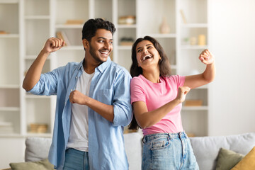 Joyful hindu spouses dancing in living room interior at home, husband and wife enjoying spending time together