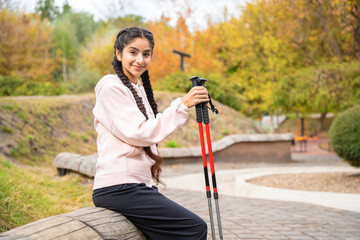 Nordic walking. Beautiful Indian woman resting with walking poles in the park.