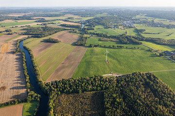 Aerial view of European village, big agriculture fields, forests, river and wind turbine