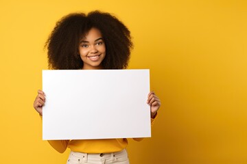 Cute young woman with a happy and excited expression holding a blank white card on a yellow background for selling information.
