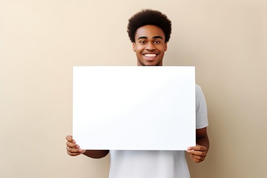 Young happy guy holding a blank white banner on a light background.