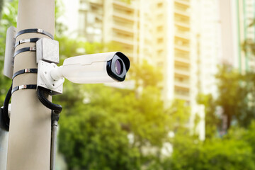 Modern public CCTV camera on an electric pole with blurred building and park background.