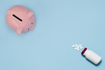 Top view of pink piggy bank with medicine bottle and pills isolated on light blue background, health care saving concept