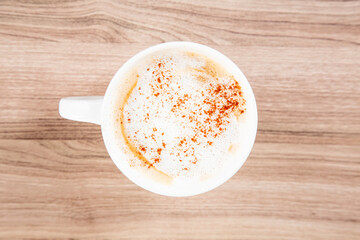 Latte in a white mug with cinnamon sprinkle on a wooden cutting board top down view