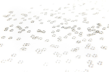 Background of silver colored jump rings scattered over white very shallow depth of field