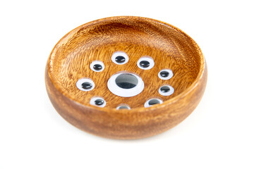Small googley eyes surround a large single eye in a wooden bowl side view