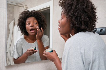 African young woman applying eco-friendly facial cream in bathroom.