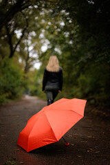 In the foreground is a red umbrella against a girl in the distance.  A red umbrella in the fall