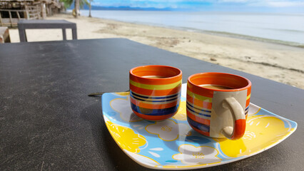 Coffee served in two colorful boho styled cups at the sunny beach, relaxing and unwinding on a summer day