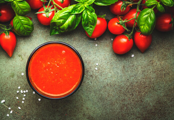 Freshly squeezed tomato juice with sea salt in glass and red cherry tomatoes on branches with green basil on rustic table, food background, top view