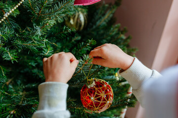 close up on child hands holding christmas tree decoration putting it on tree