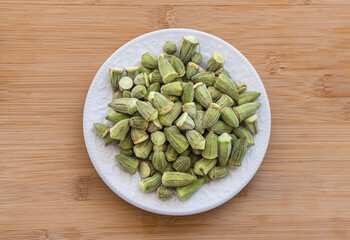 Okra cleaned and prepared for cooking. in a white porcelain plate. wood patterned background.