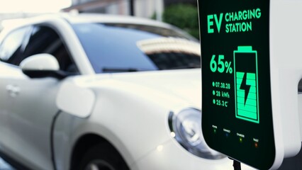 EV charging station display battery status interface for electric car, exemplifying green city with clean energy. Technological advancement of alternative energy sustainability utilization. Peruse