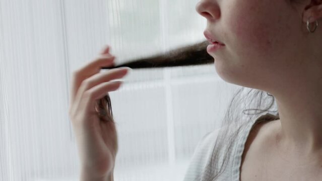 Anxious Caucasian woman curls lock of hair on her finger. Close-up of hand and face. Concept of psychological disorder ocd and mental problem